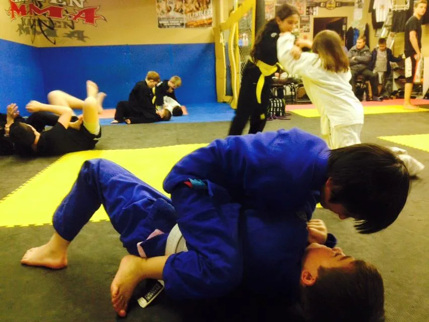 Kids grappling in gis on the yellow and blue mats